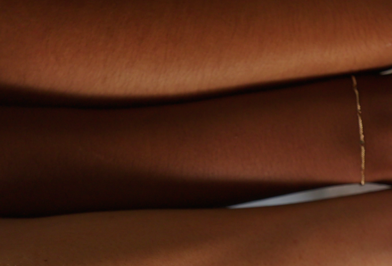 Close-up of a wrist wearing a delicate thin gold chain bracelet against brown skin.