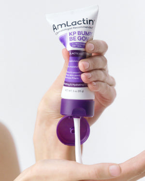 Pair of hands squeezing AmLactin KP Bumps Be Gone Cream Tube into the palm of one hand.