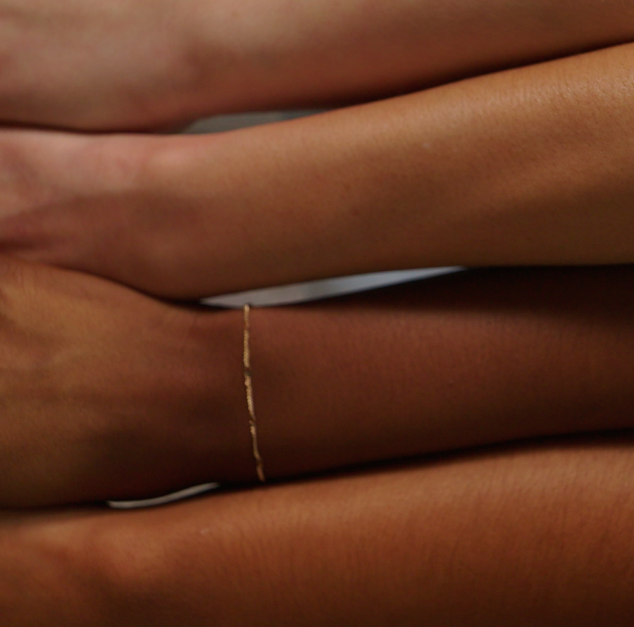 Close-up of a wrist wearing a delicate thin gold chain bracelet against brown skin.