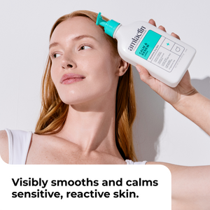A woman with light skin and long strawberry-blonde hair holds a bottle of Amlactin Calm & Renew to her forehead. The bottle is white with a bright teal cap and label.