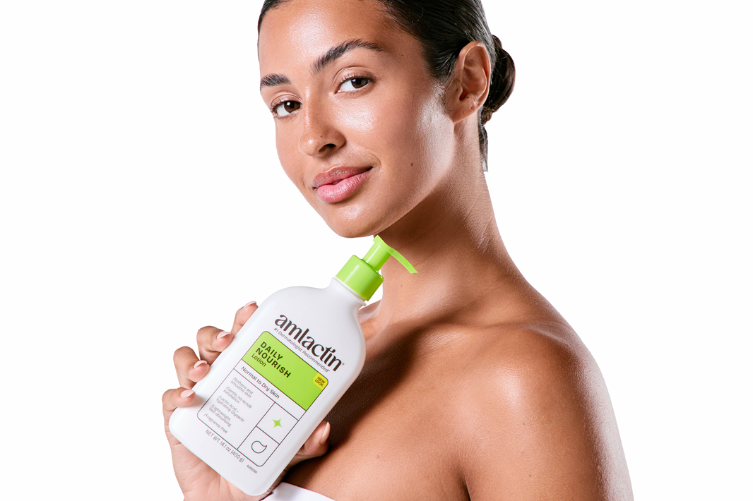 A woman holding Amlactin bottle with a green pump against a solid white background.